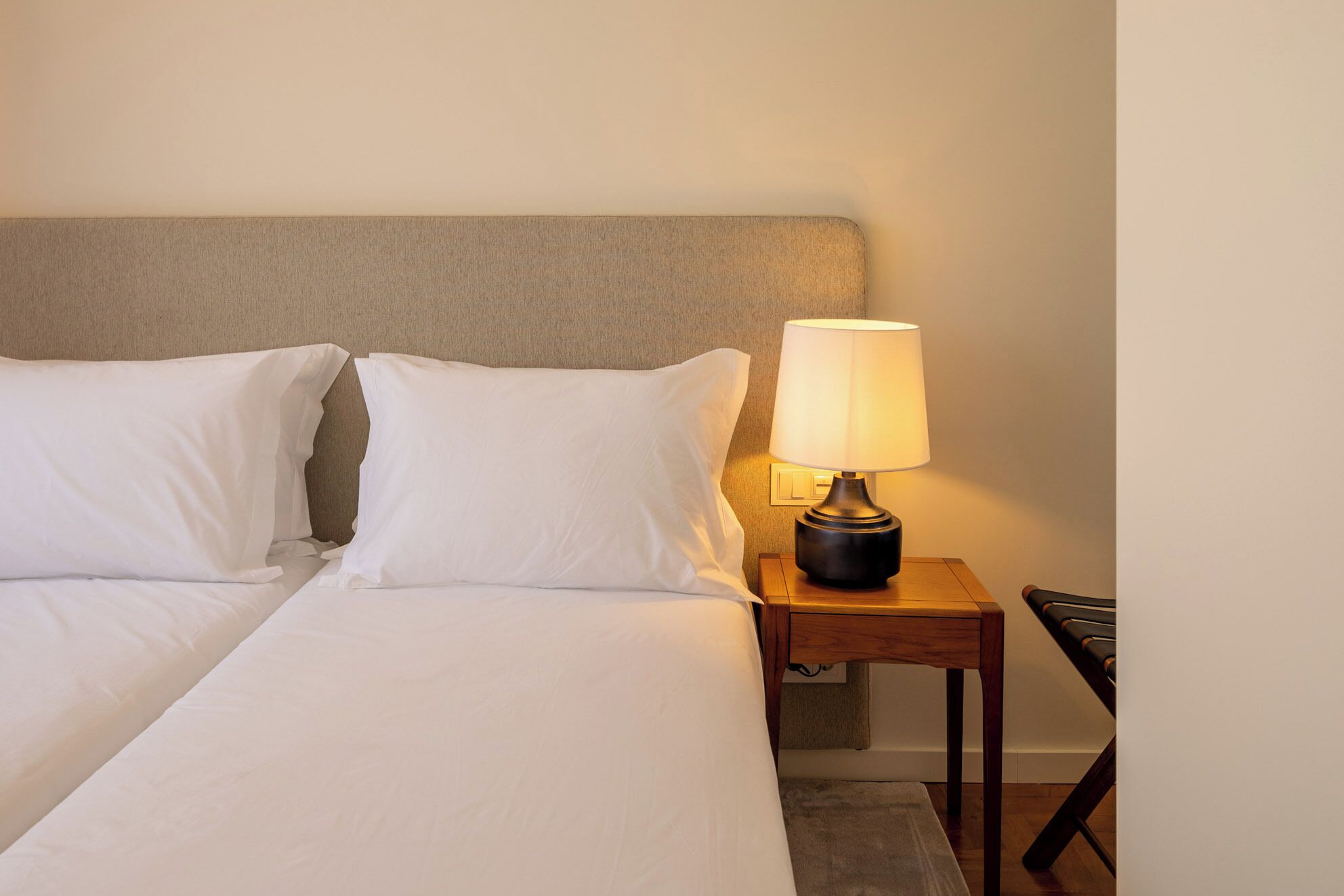 Une chambre d’hôtel avec un lit, deux oreillers, une table de chevet avec une lampe et une petite table de nuit en bois.