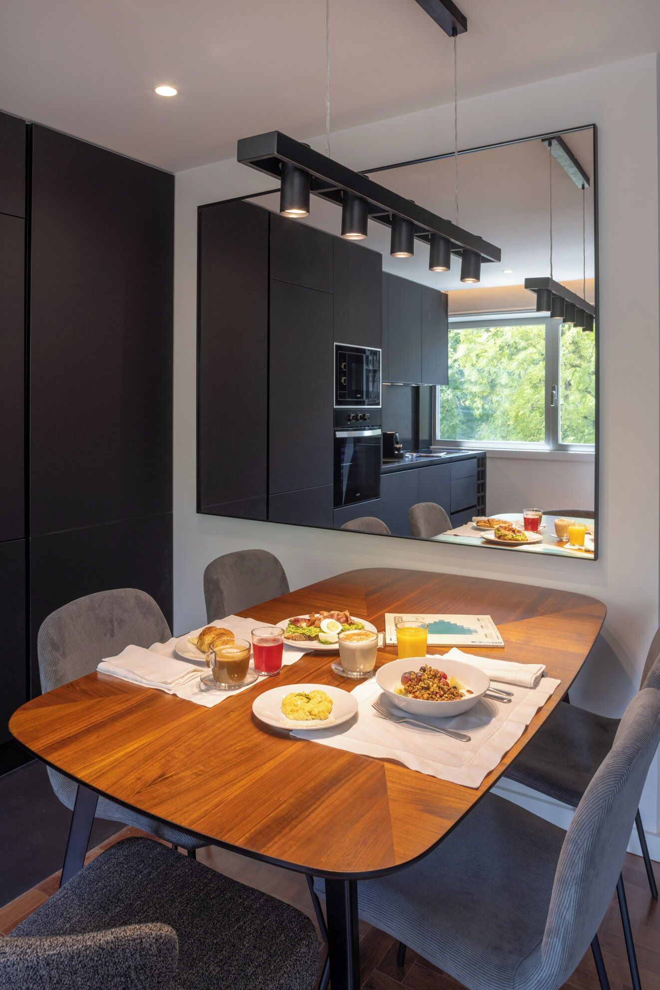Un comedor moderno con una mesa de madera dispuesta para el desayuno, un espejo grande y vistas al exterior.