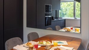 A modern dining area with a wooden table set for breakfast, a large mirror, and a view of the outdoors. - 2-Bedrooms in Avenidas Novas with Balcony, Services and the Comfort of Home (Lisboa)