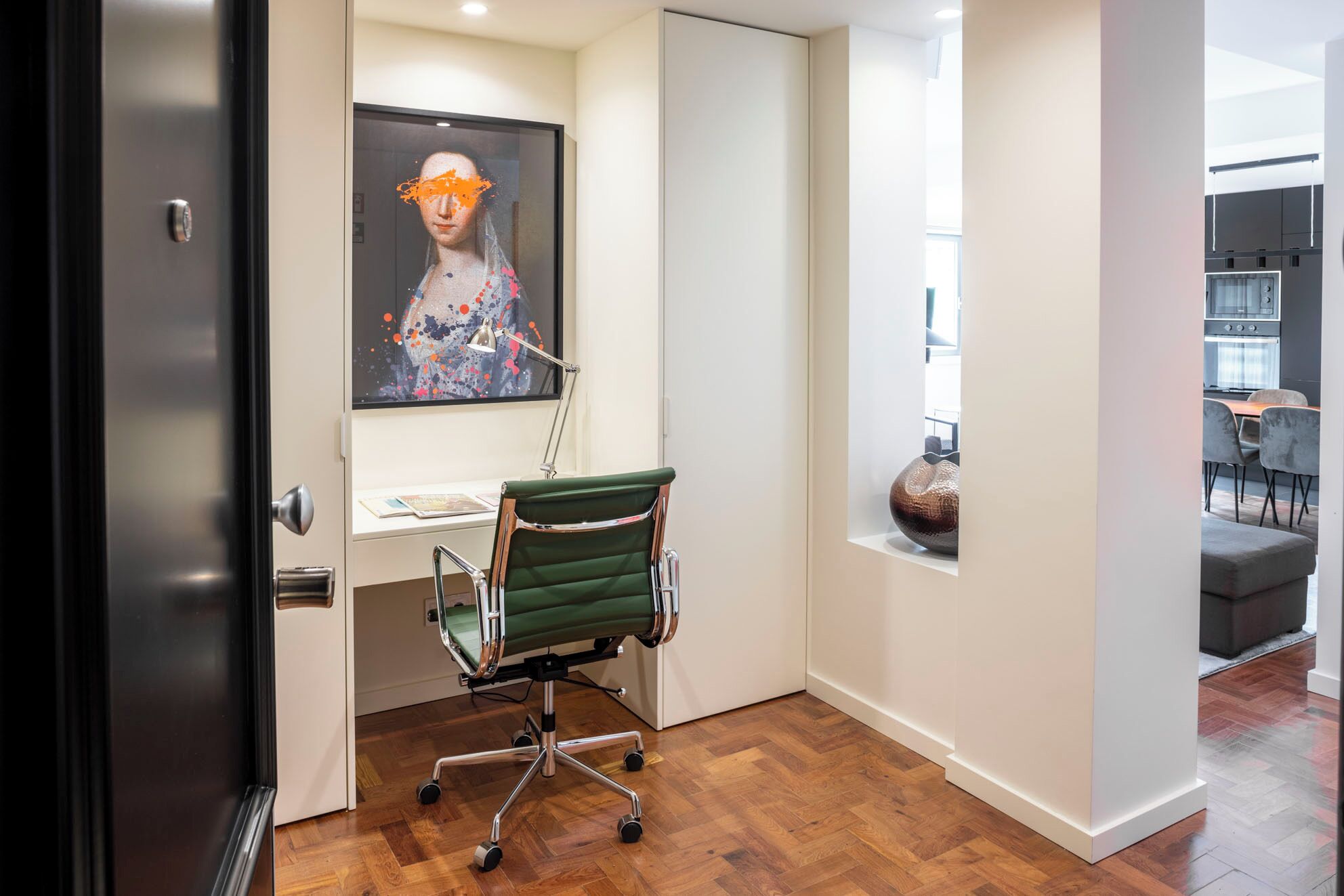 Un espacio de oficina moderno con una silla de escritorio verde, un escritorio con una lámpara y un cuadro en la pared.