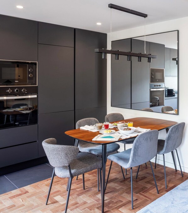 A modern kitchen with dark cabinetry, a wooden dining table, and a large mirror reflecting the kitchen area.