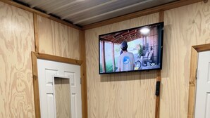 A room with wooden panel walls, a quilted bedspread, a television mounted on the wall, and a door with a mirror.