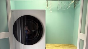 A compact laundry room with two stacked washing machines, a drying rack, and a small wooden shelf.