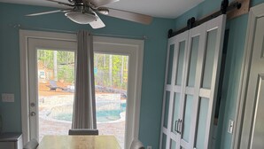 A dining area with a wooden table and chairs, a ceiling fan, and a view of a swimming pool through a glass door.