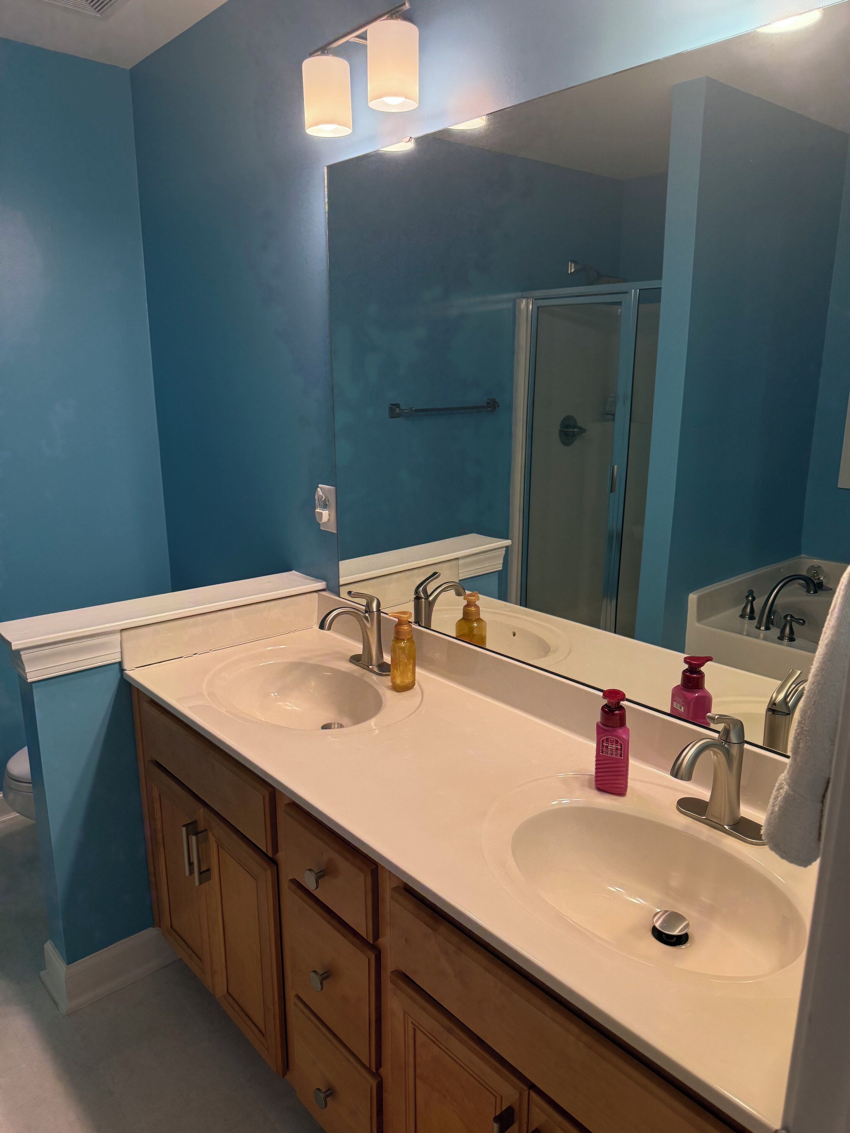 A bathroom with two sinks, wooden cabinets, a large mirror, and a glass shower door.
