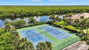 A tennis court with two courts, surrounded by lush greenery and a body of water.