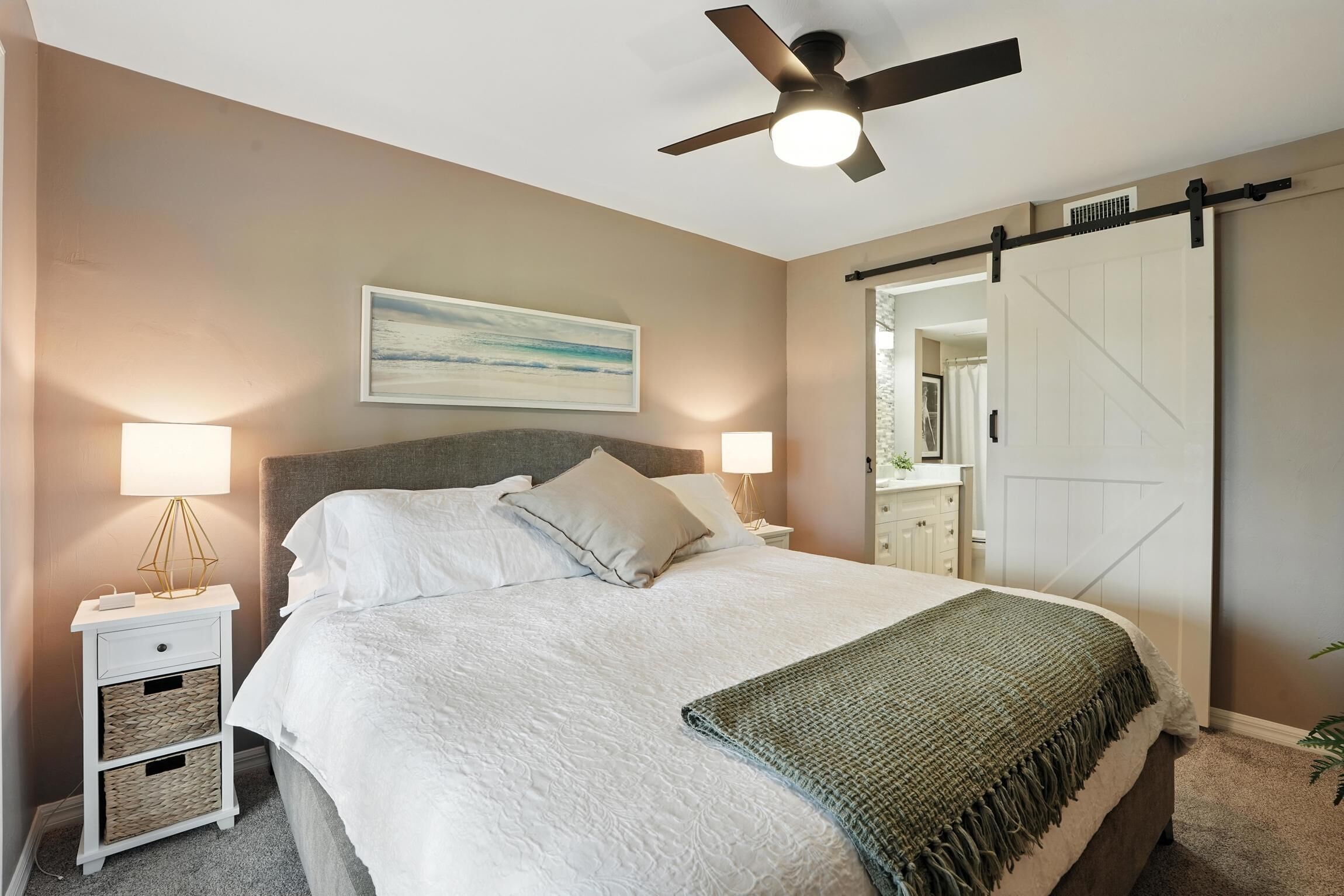 A bedroom with a bed, nightstands, a ceiling fan, a sliding barn door, and a painting on the wall.
