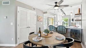 A dining area with a round table, chairs, a ceiling fan, and a kitchen in the background.