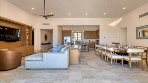 Un vaste espace de vie comprenant un grand canapé, un téléviseur et un coin repas avec des chaises en bois et un sol en marbre.
