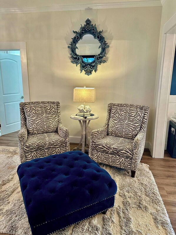 Una sala de estar con dos sillones a rayas de cebra, una mesita redonda con lámpara y un reposapiés capitonado.