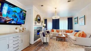 Una sala de estar con chimenea, un conjunto de sofás, un televisor y un espejo decorativo.