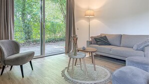 A modern living room with a grey sofa, a grey armchair, a small round table, and a floor lamp. There is a large window with curtains, and a view of greenery outside. - Beautiful home in Hoeven with WiFi (Hoeven)