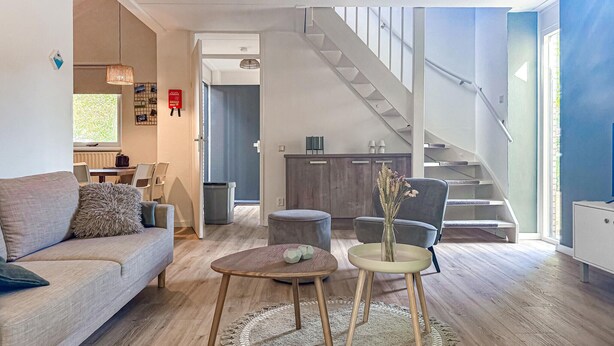 A modern living room with a sofa, coffee table, and chairs, a staircase, and a view of the outdoors. - Beautiful home in Hoeven with WiFi (Hoeven)