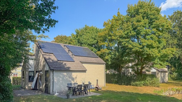 A small, single-story building with a sloped roof, solar panels, and a patio with outdoor furniture. - Beautiful home in Hoeven with WiFi (Hoeven)