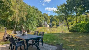 An outdoor patio with a table and chairs, surrounded by lush greenery and a pond. - Beautiful home in Hoeven with WiFi (Hoeven)
