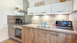 A modern kitchen with wooden cabinets, a built-in oven, a stove, a microwave, and a sink with two bottles of hand soap. - Beautiful home in Hoeven with WiFi (Hoeven)