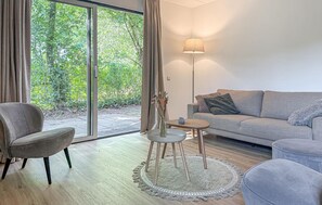 A modern living room with a grey sofa, a grey armchair, a small round table, and a floor lamp. There is a large window with curtains, and a view of greenery outside. - Beautiful home in Hoeven with WiFi (Hoeven)