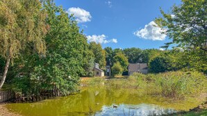 A serene pond surrounded by lush greenery and a modern building with a tiled roof. - Beautiful home in Hoeven with WiFi (Hoeven)