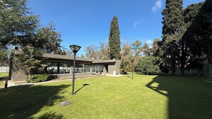 Um edifício moderno com telhado plano, rodeado por relvado bem cuidado e árvores.