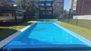 Piscina retangular com interior azul, rodeada por uma área gramada e uma cerca preta.