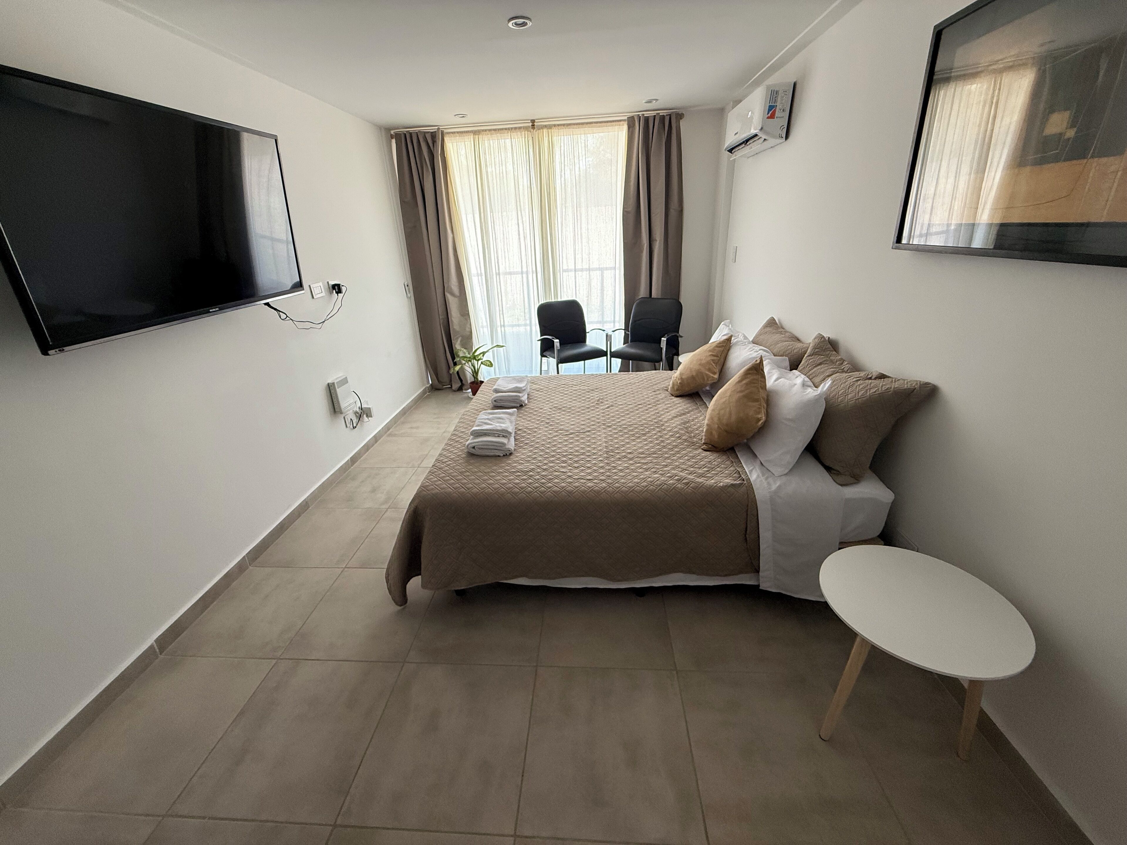 Et hotelværelse med seng, fjernsyn, et lille bord og en stol.