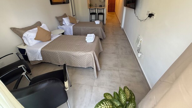 Quarto de hotel com duas camas, uma escrivaninha, uma cadeira, um vaso de planta e uma televisão fixada na parede.