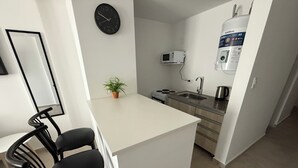 Cozinha moderna com bancada branca, relógio preto, micro-ondas, chaleira e dispensador de água.