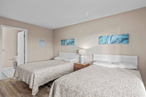 A hotel room with two beds, a nightstand with a lamp, and a door leading to a bathroom.
