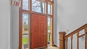 A wooden staircase with a handrail leading to a red door with glass panels. - 🛶 Torch Lake Vista | A-Ga-Ming Golf Retreat | Sunrise Views + Dual-Unit Condo ➠ 741 (Kewadin)