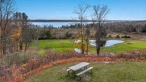 A golf course with a pond, a picnic table, and a view of a lake. - 🛶 Torch Lake Vista | A-Ga-Ming Golf Retreat | Sunrise Views + Dual-Unit Condo ➠ 741 (Kewadin)