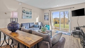 A spacious living room with a large sofa, a wooden coffee table, and a TV mounted on the wall. - 🛶 Torch Lake Vista | A-Ga-Ming Golf Retreat | Sunrise Views + Dual-Unit Condo ➠ 741 (Kewadin)