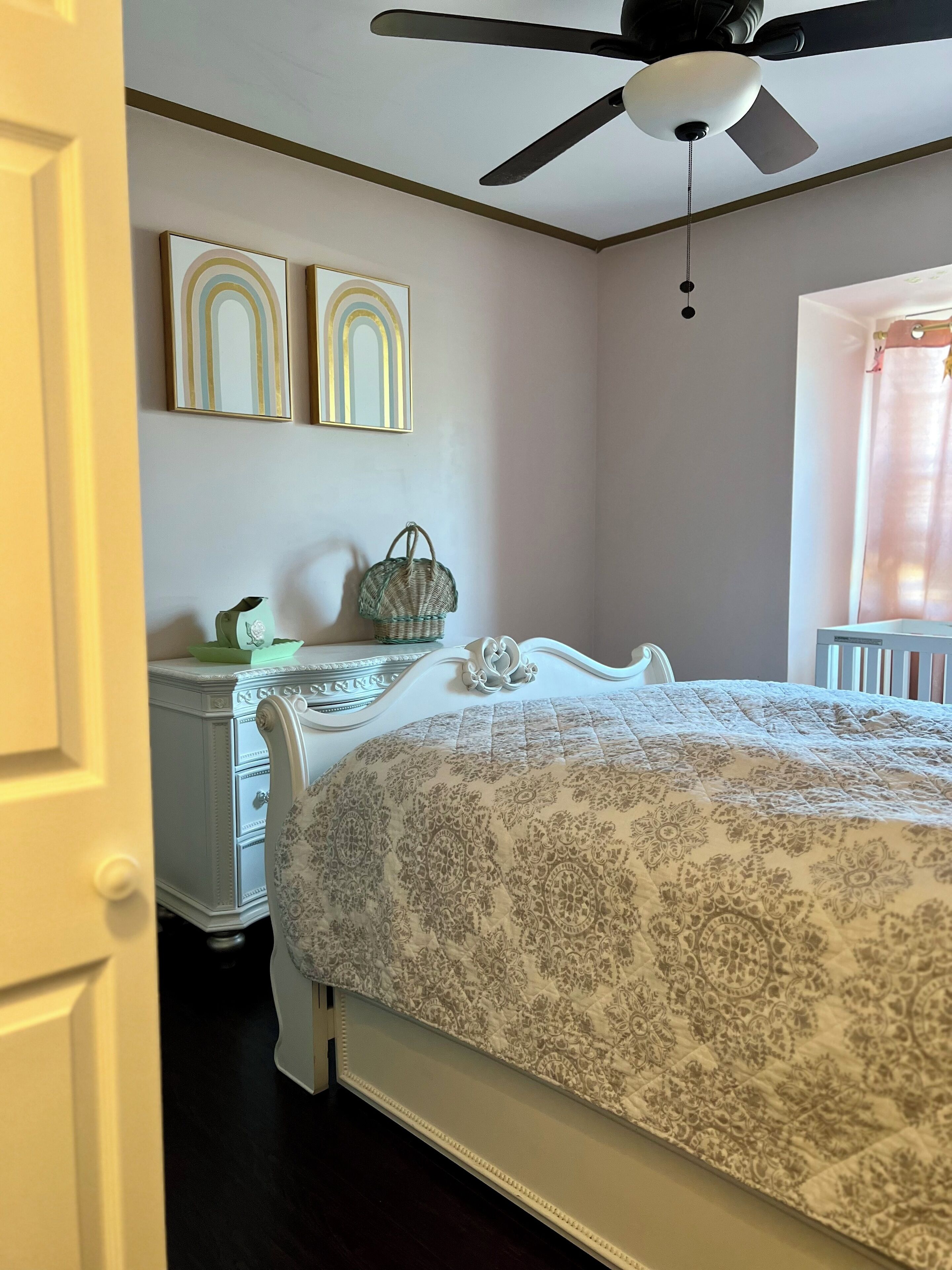 Een slaapkamer met een bed, een kaptafel, twee decoratieve wandpanelen, een plafondventilator en een raam met gordijn.