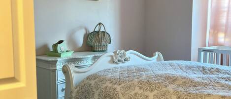 Een slaapkamer met een bed, een kaptafel, twee decoratieve wandpanelen, een plafondventilator en een raam met gordijn.