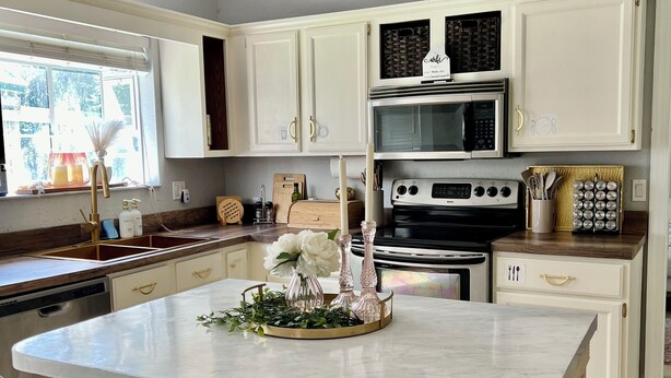 A modern kitchen with white cabinets, a central island with bar stools, a chandelier, and a large window.