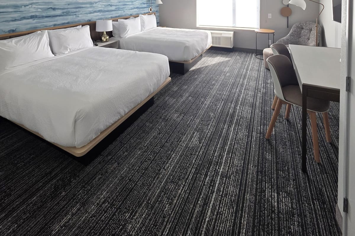 A hotel room with two beds, a desk, and a chair.