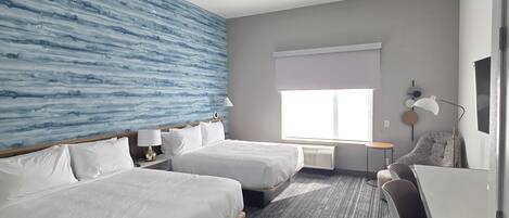 Habitación de hotel con dos camas, un escritorio y una silla.