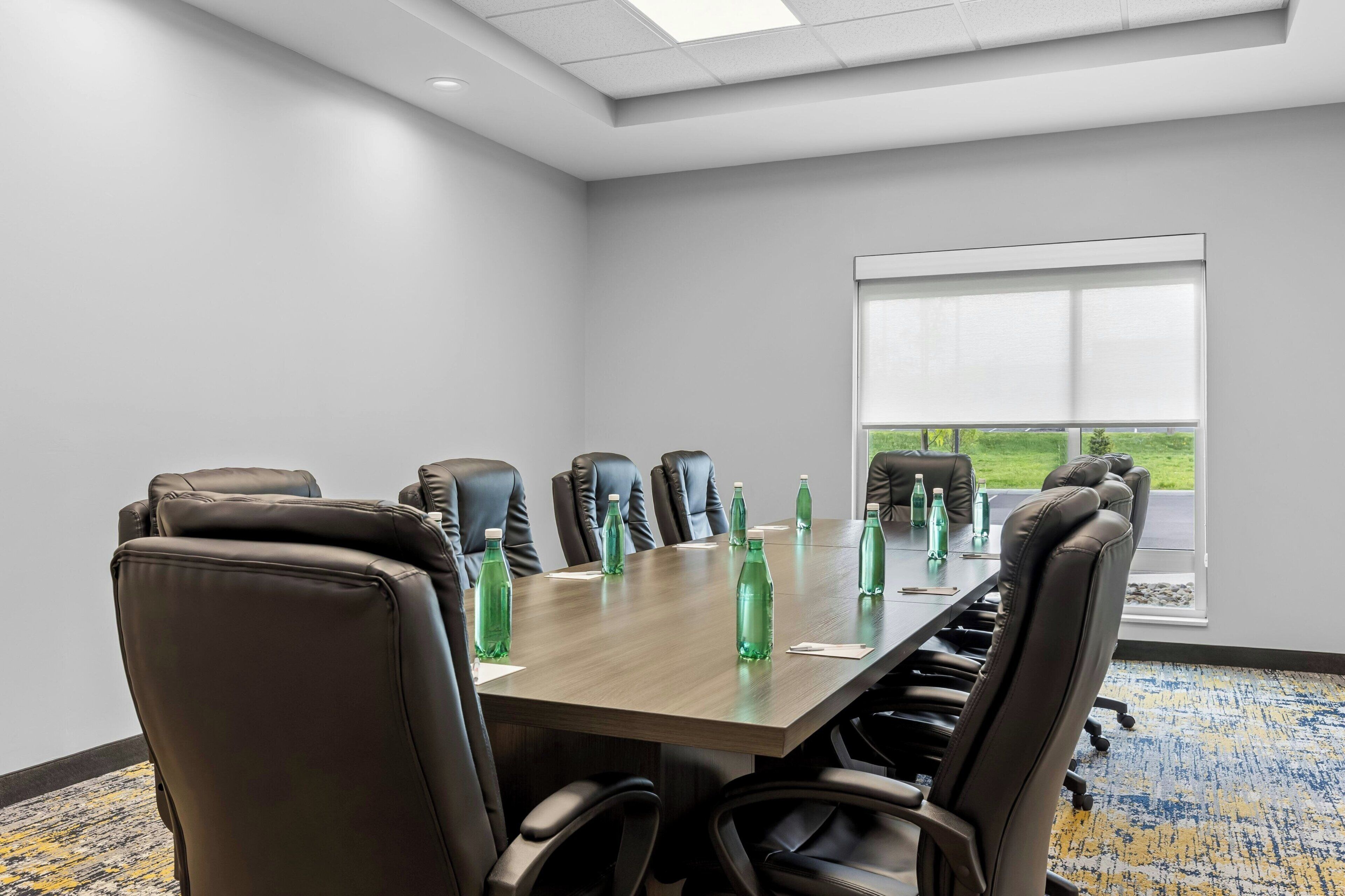 Une salle de conférence avec une longue table, de nombreuses chaises et des bouteilles vertes.