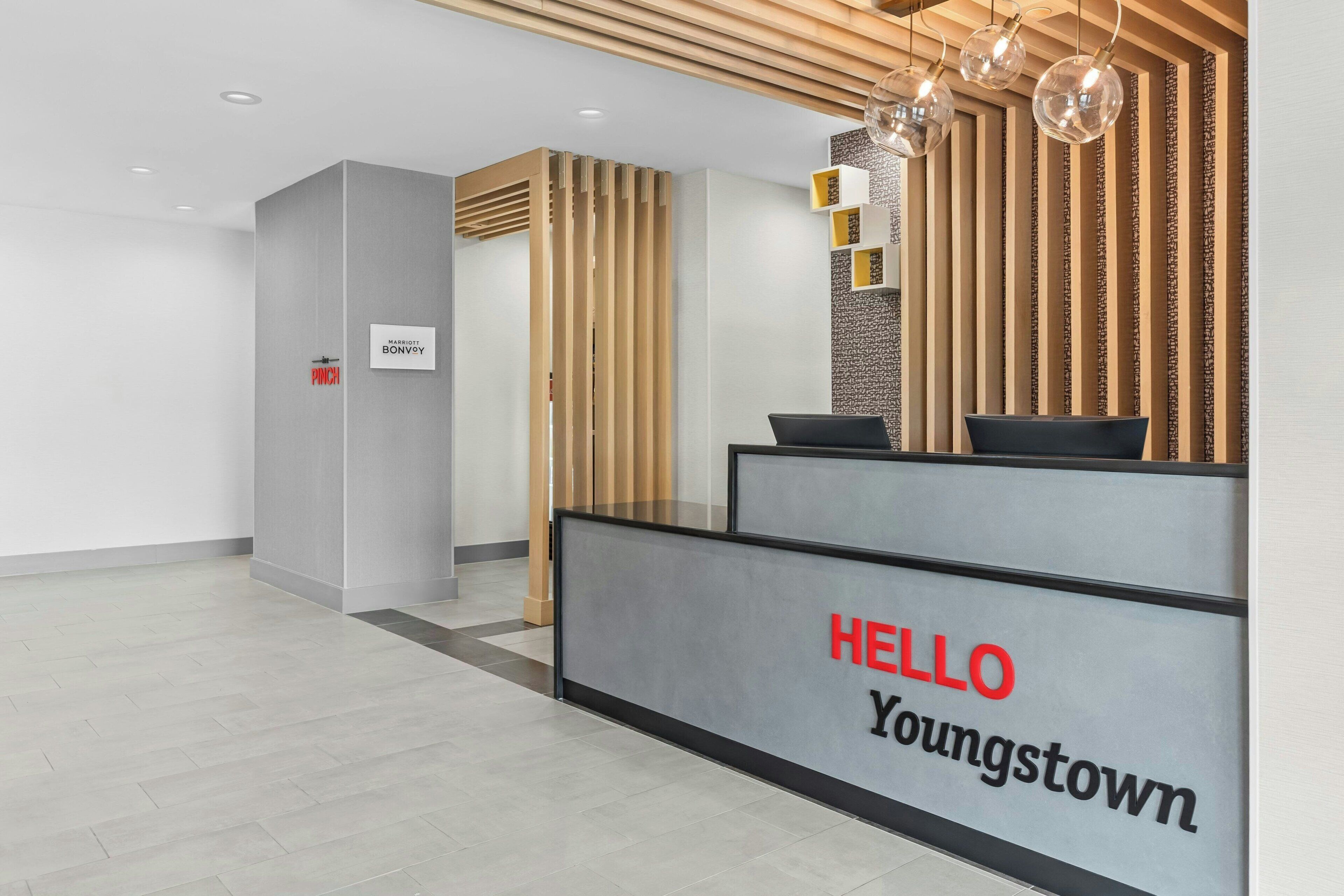 A reception desk with a 'HELLO Youngstown' sign, a vertical wooden slat wall, and a modern light fixture.