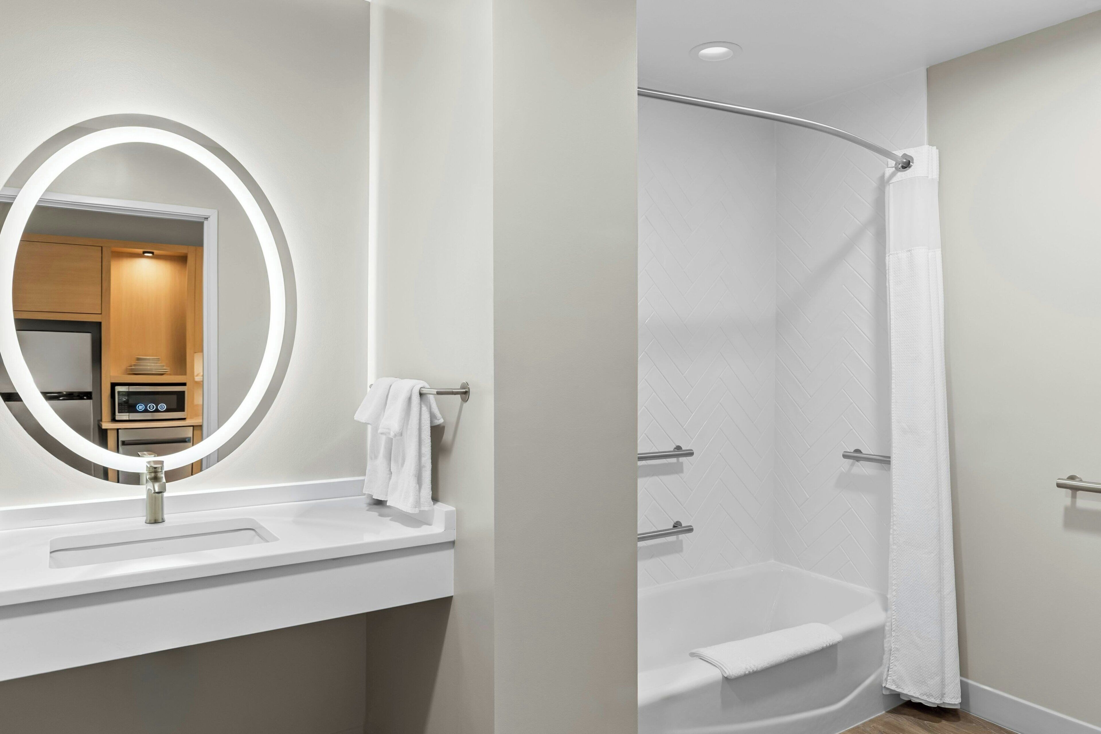 Une salle de bain moderne avec un lavabo blanc, un miroir doté d’un éclairage circulaire et une douche avec un rideau blanc.