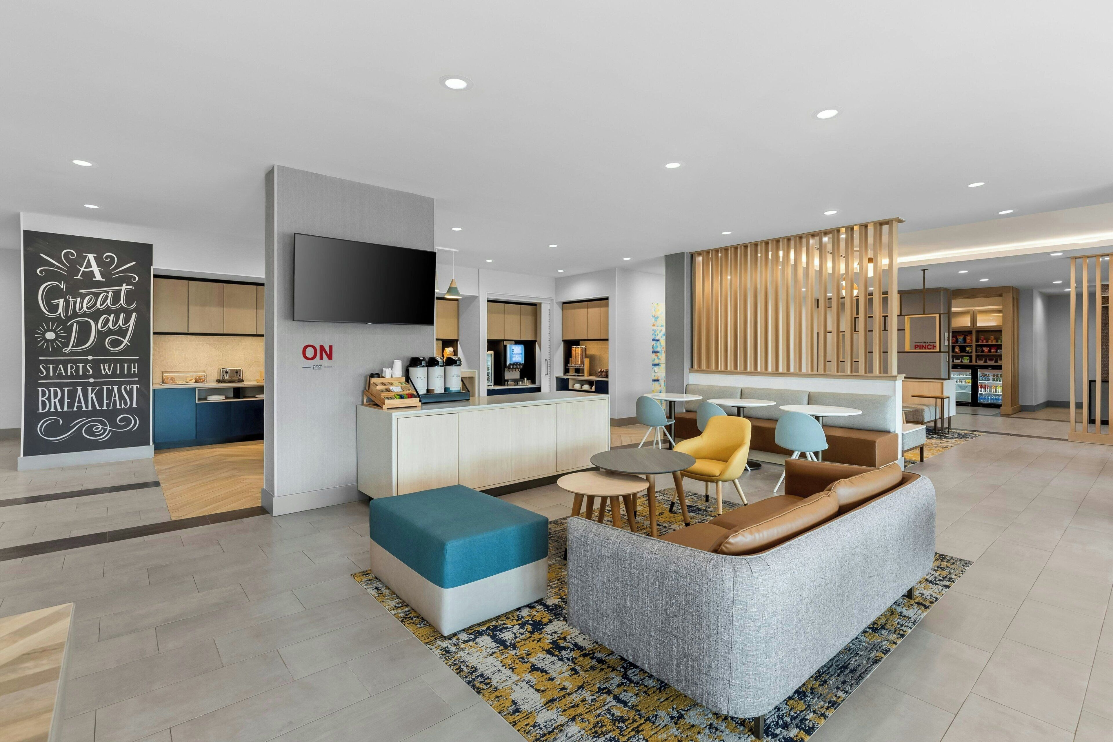 A modern hotel lobby with a flat-screen TV, a sofa, a coffee table, and a sign that reads 'A Great Day Starts with Breakfast.'