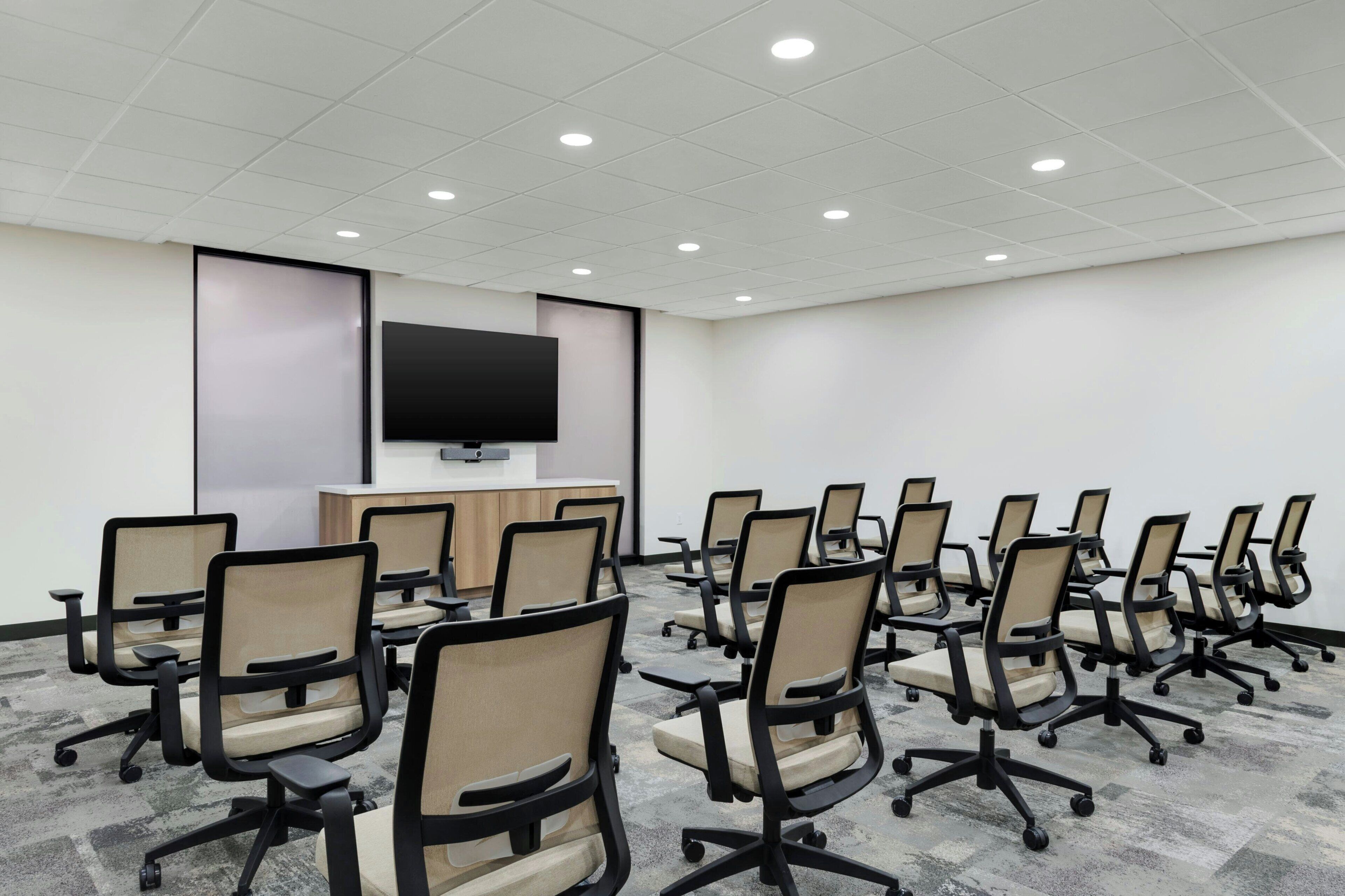 A conference room with rows of office chairs, a flat-screen TV on a stand, and a carpeted floor.