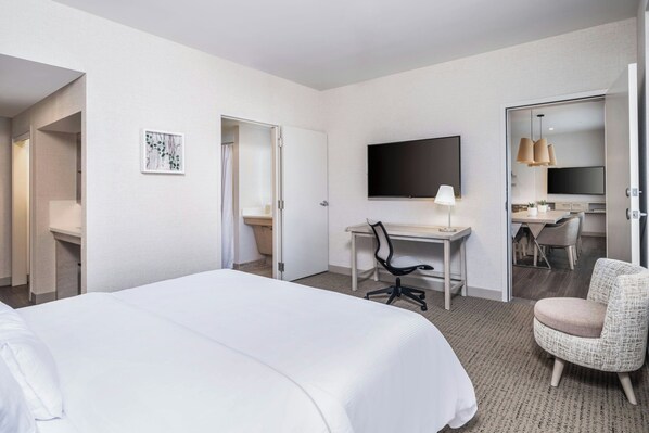 Una habitación de hotel con una cama grande, un escritorio con una silla, un televisor y un área de descanso con una silla.