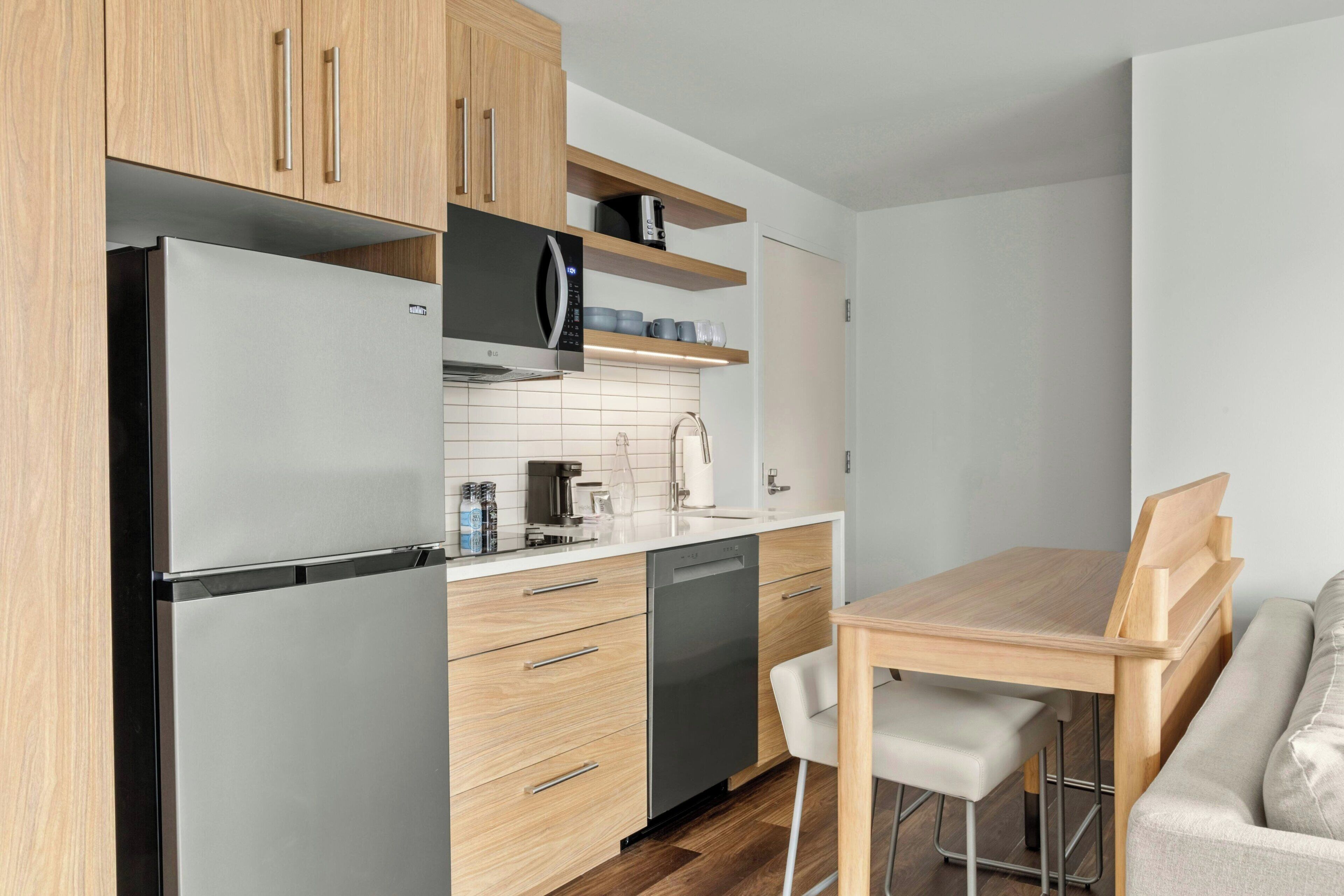 A modern kitchen with a refrigerator, microwave, and dishwasher, wooden cabinets, and a dining area with a table and chairs.