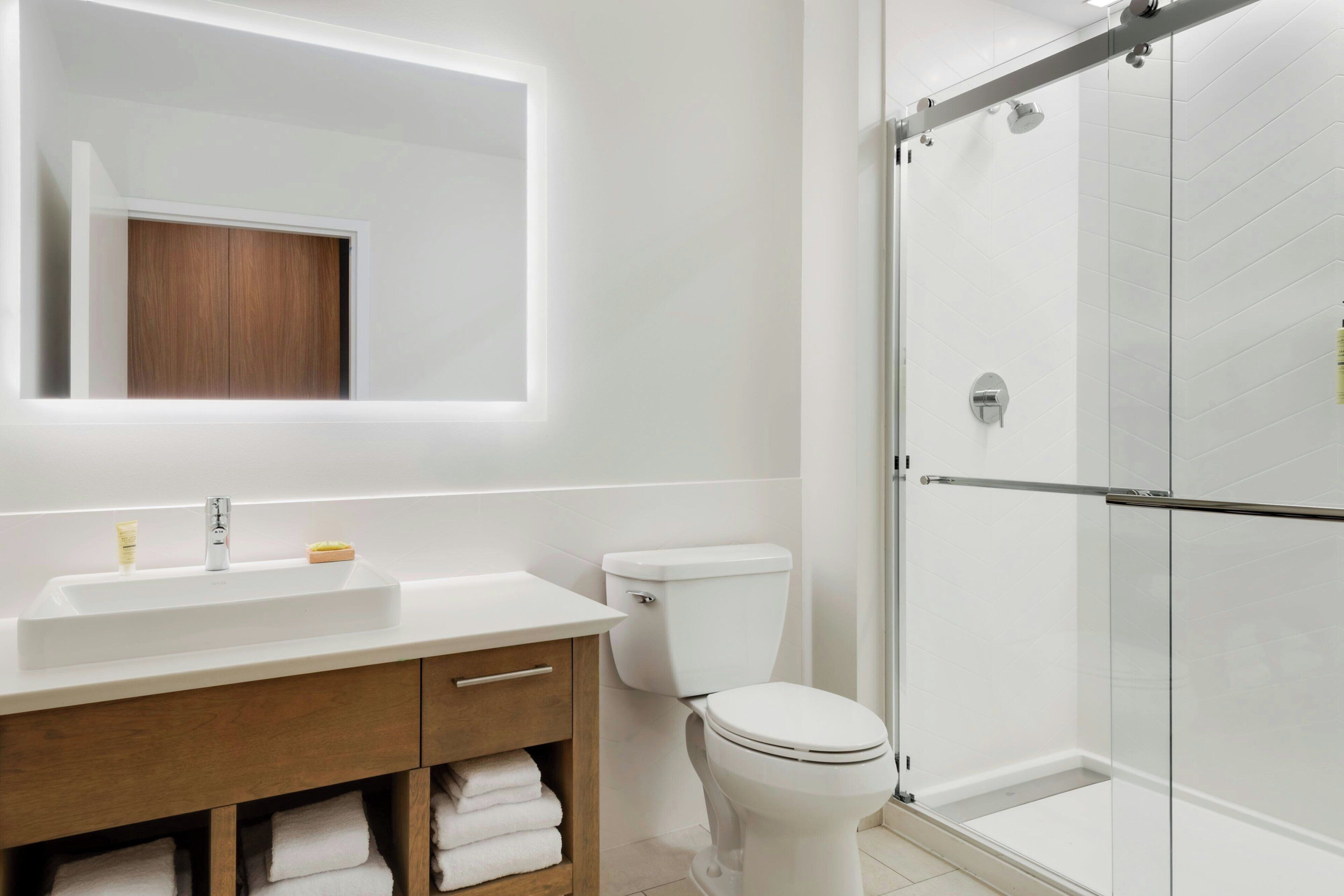 A modern bathroom with a white sink, wooden vanity, a toilet, and a glass shower enclosure.
