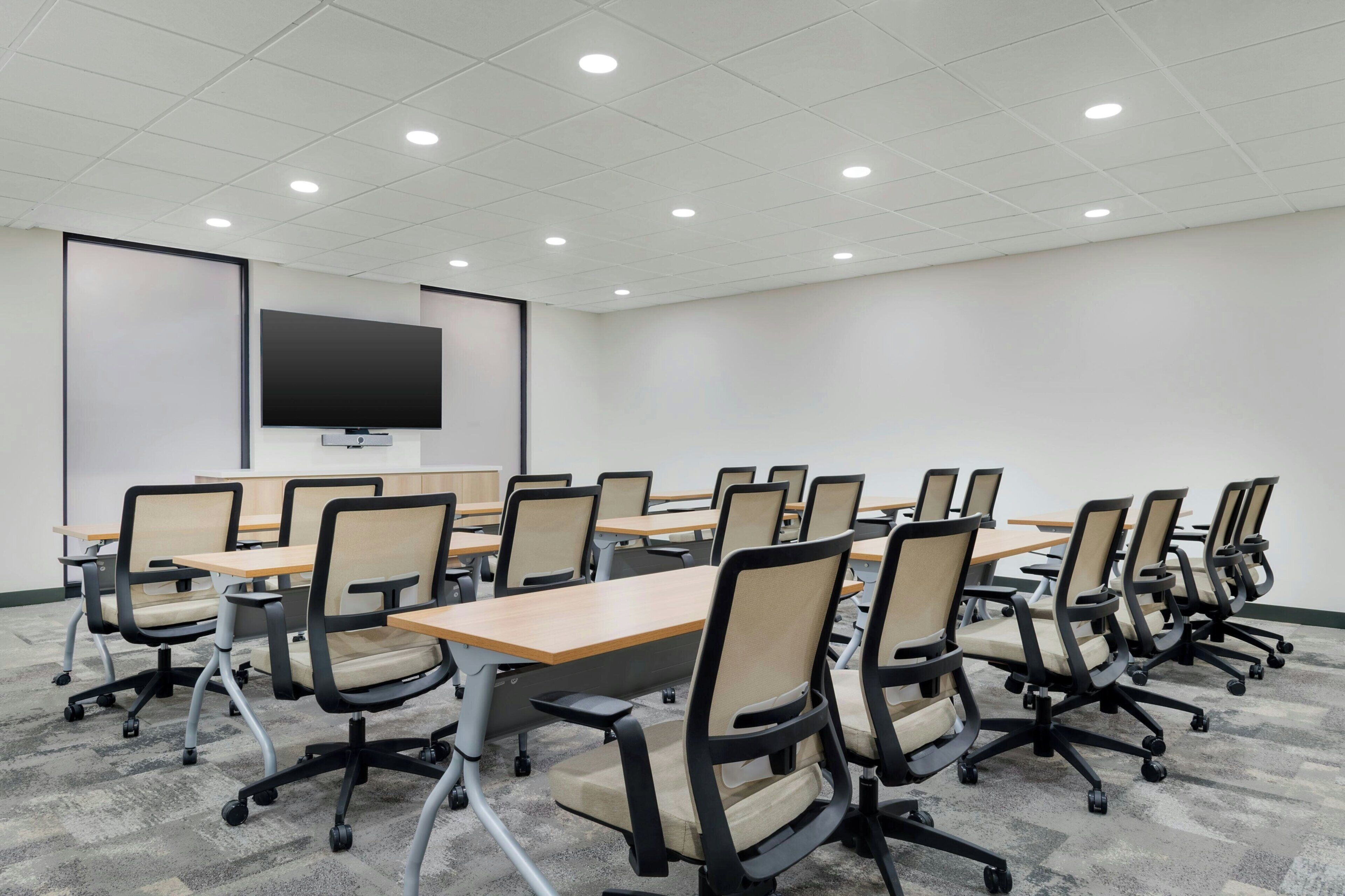 Une salle de conférence avec des rangées de chaises, des tables, un grand écran et des luminaires au plafond.