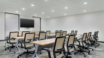Une salle de conférence avec des rangées de chaises, des tables, un grand écran et des luminaires au plafond.