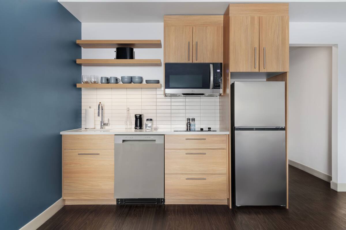 A modern kitchen with wooden cabinets, a stainless steel refrigerator, a microwave, and a dishwasher.