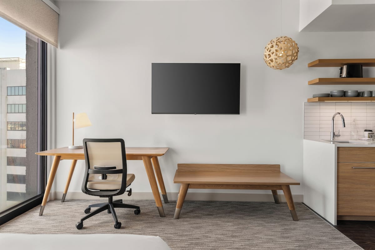 A modern room with a desk, office chair, bench, and a mounted TV.