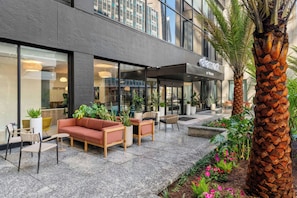 Un edificio moderno con un café llamado 'element', con terraza amueblada con sofás y sillas, plantas en macetas y una palmera.