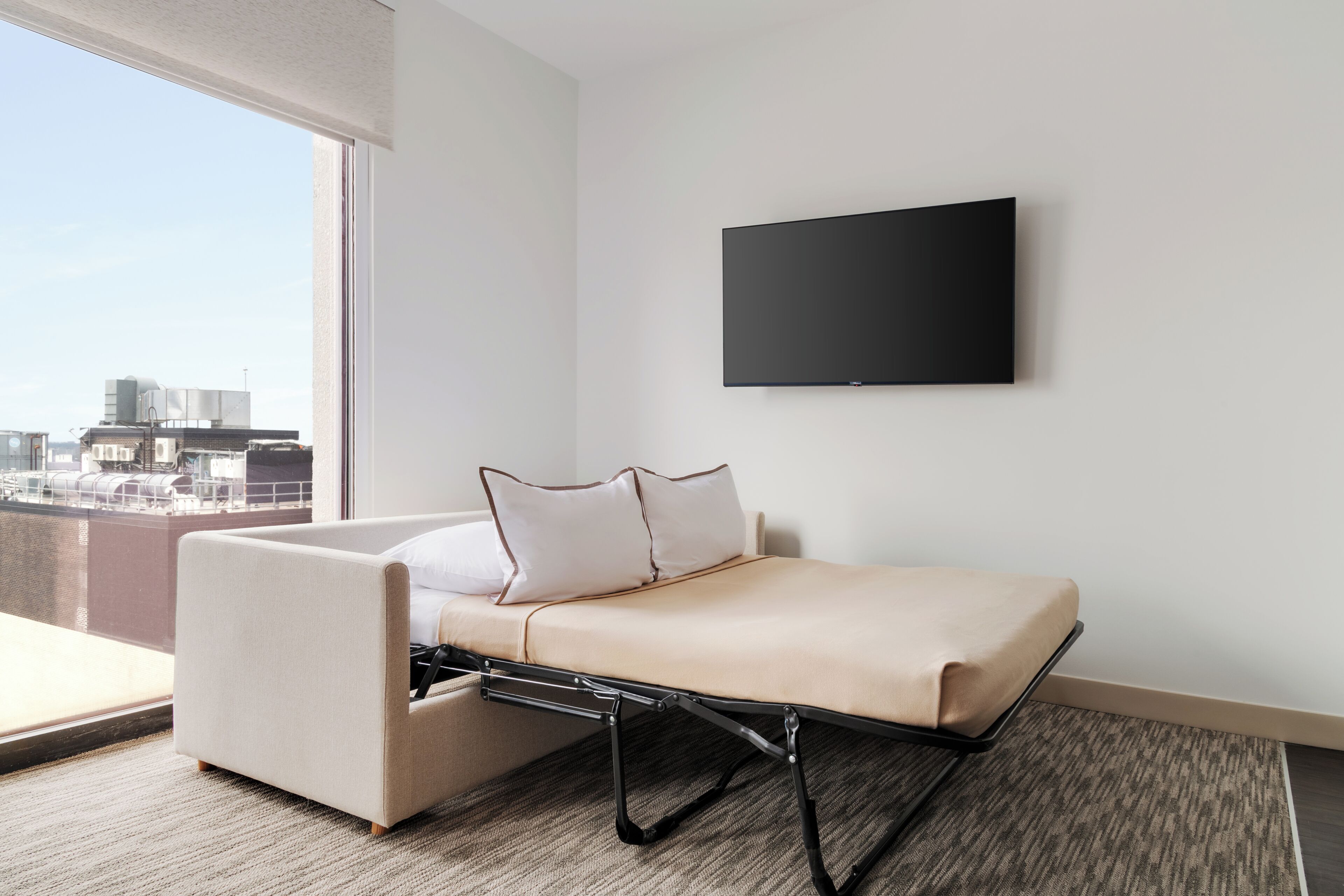 Una moderna camera d'hotel con un letto, una TV a parete e vista sulla città attraverso la finestra.